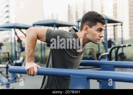 Handsome young man doing dips on the uneven bars on the outdoor sports field. Healthy lifestyle, sports and endurance concept. Stock Photo
