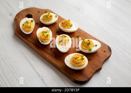 Homemade Deviled Eggs with Chives on a rustic wooden board on a white wooden background, side view. Stock Photo