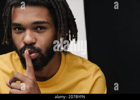 Photo of a african guy posing isolated over black and white wall background showing silence gesture Stock Photo