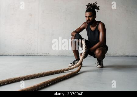 Image of athletic african american sportsman working out with battle ropes indoors Stock Photo
