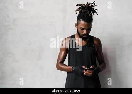 Image of serious african american sportsman using cellphone while standing indoors Stock Photo