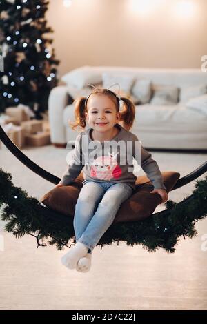 Adorable little girl on Christmas swing. Christmas tree. Stock Photo