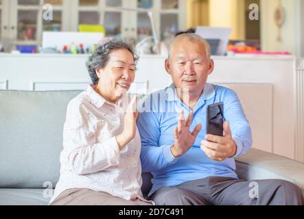 Happy Asian Senior Couple Making Video Call On mobile Phone at home Stock Photo