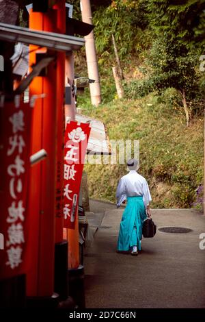 Kyoto/Japan - 2016 Nov 22 : Men dress like Shinto priests, wearing white shirts and green pants. Rear view, walking on a walkway in Fushimi Inari Shri Stock Photo