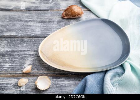Empty blue ceramic plate on gray wooden background and blue textile. Side view, close up. Stock Photo