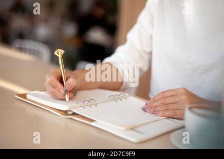 Well-groomed woman hands is writing in diary with stationery supplies ...