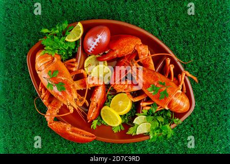 Two ready to eat red lobsters with lemon on football ball plate on grass background. Stock Photo
