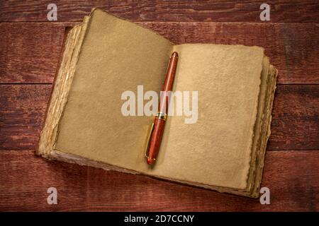 antique leatherbound journal with decked edge handmade paper pages and a stylish pen on a rustic wooden table, journaling concept Stock Photo