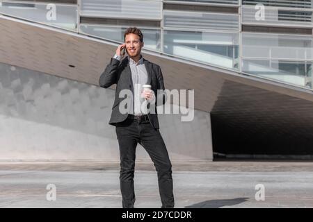 Young business man calling talking on the mobile phone on coffee break from office building outside. Businessman walking on street commute lifestyle Stock Photo