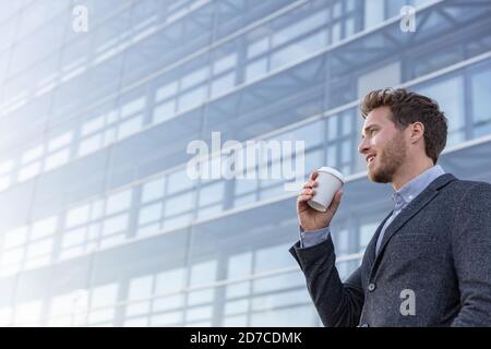 Happy young business professional man drinking coffee cup on his morning commute walk to work. Caucasian businessman with hot drink on office Stock Photo