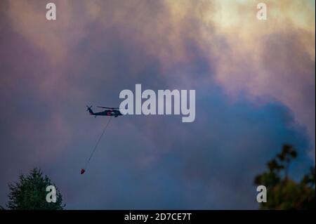 Aerial firefighting helicopter with fire bucket flying into smoke to drop water on wildfire Stock Photo