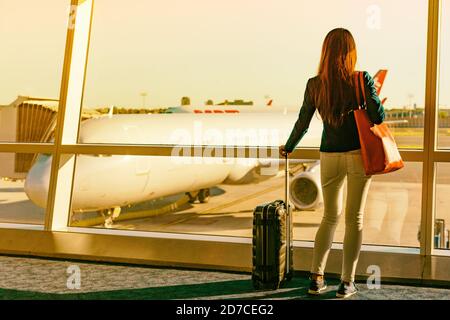 Airport travel woman looking through window sunset at airplanes on tarmac waiting for flight departure leaving for business trip holiday at first Stock Photo