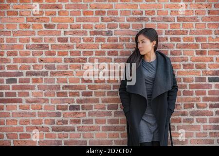 Beautiful Asian fashion model woman wearing fall outdoor wool jacket on urban brick wall background in city outdoors for autumn lifestyle Stock Photo