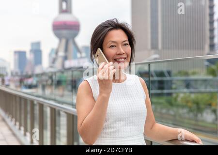 Phone Asian woman mature middle age chinese businesswoman talking business on mobile smartphone call outside on Shanghai street with Pearl tower in Stock Photo