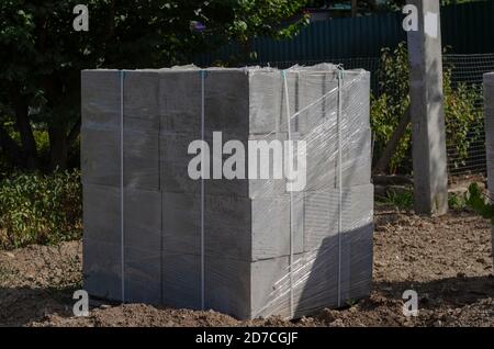 Gray cement blocks on wooden pallet at  side of road. Packaging of building materials fastened with bandage tapes with stretch film. Delivery of build Stock Photo