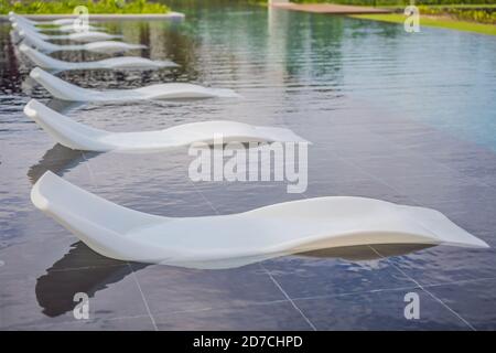 White sun loungers stand in the pool water Stock Photo