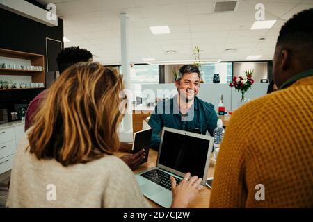 Female typing on laptop while colleagues chat during lunch break in office foyer before business meeting Stock Photo