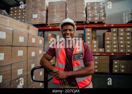 Male factory worker smiling besides packages in warehouse  Stock Photo
