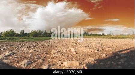 Low angle view of rural stone road and trees at sunset.Abstract landscape with orange sky and white clouds. Stock Photo