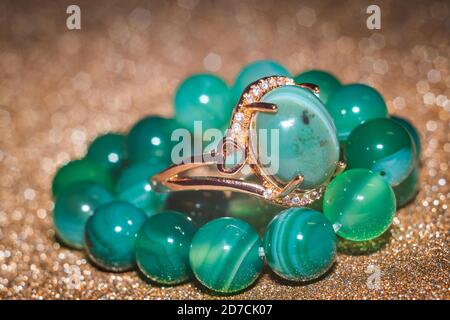 Modern gold ring and beaded bracelet made from green striped agate on glitter background. Stock Photo