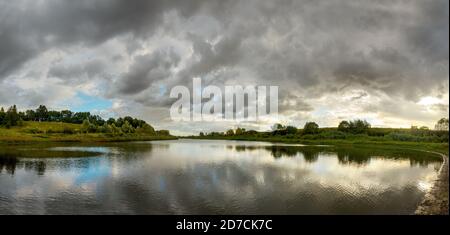 Stormy dramatic sky landscape with calm lake and grey clouds during sunset Stock Photo