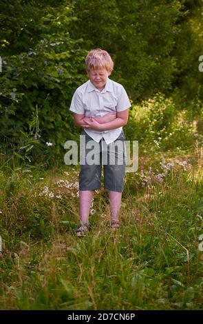 The boy holds his stomach and winces in pain in the Park Stock Photo