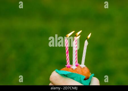 Mini cupcake with four candle for four year anniversary isolated on green background.Anniversary celebration.Congratulations card. Burning candles Stock Photo