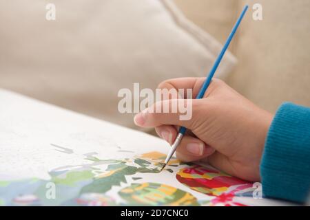 13 - Plenty of copy space in this painting by numbers activity photo. Gentle young hand uses vivid paintbrush and colors to create the artwork Stock Photo