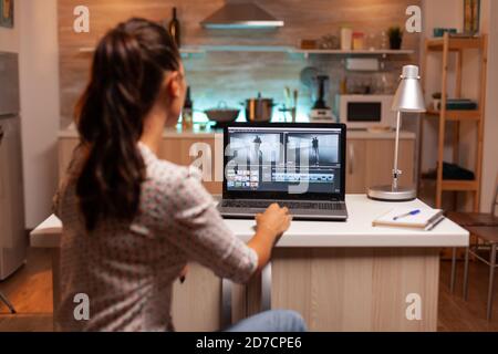 Back view of creative filmmaker working on a movie on laptop during midnight. Content creator in home working on montage of film using modern software for editing late at night. Stock Photo
