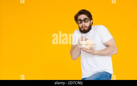 Portrait vogue young man in 3d glasses, white t-shirt watching movie film, holding popcorn, cup of soda isolated on bright yellow background. People Stock Photo