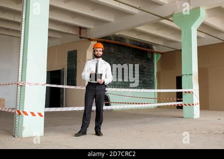 A young bearded Architect in a construction helmet on a construction site checks the result Stock Photo