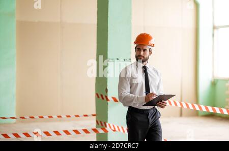 A young bearded Architect in a construction helmet on a construction site checks the result Stock Photo