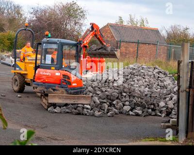 Workmen using Bob Cat  excavator to load broken rock into a dumper truck Stock Photo