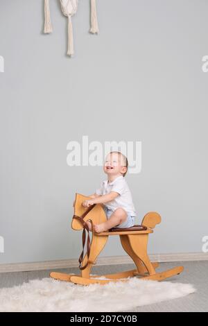 Child Sitting On Ride On Toy In Playroom. Toddler Baby Boy Riding Swinging On Rocking Chair Toy Horse Stock Photo