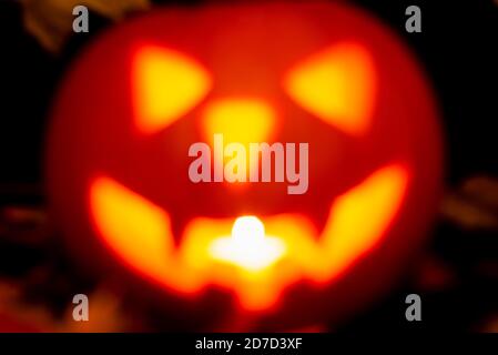 Blurred image glowing lantern-Jack carved pumpkin for Halloween holiday with burning candle inside close-up in the dark, isolated black background. Stock Photo
