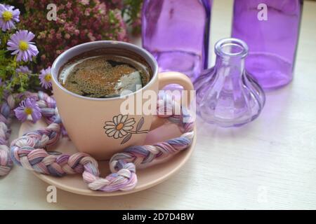 Hot dark coffee in a vintage cup and on an old white wooden background with violet flowers and purple bottles Stock Photo