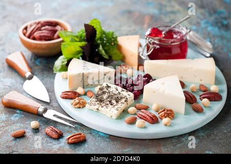 Various types of cheese on a wooden plate with jam, nuts and dried cranberries, selective focus Stock Photo