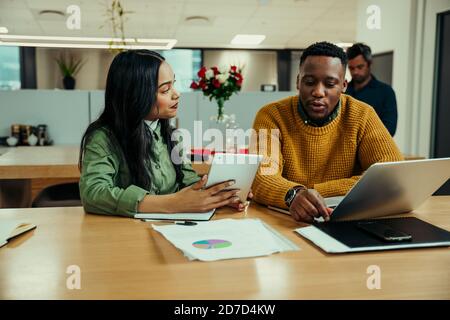 Indian woman working off digital tablet discussing work with mixed race man typing on laptop in office Stock Photo