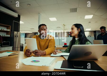 Indian woman and business man chatting during lunch break researching on laptop and digital tablet in office foyer Stock Photo