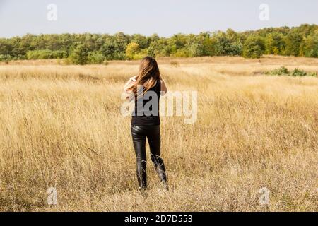 Beautiful young dark haired woman in black clothes stand in field. Stock Photo