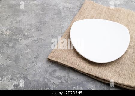 Empty white plate on gray concrete background and linen textile. Side view, copy space. Stock Photo