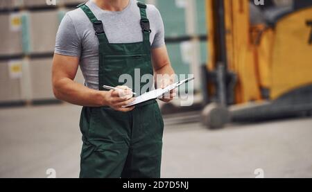 Storage worker in green colored uniform and notepad in hands checks production Stock Photo