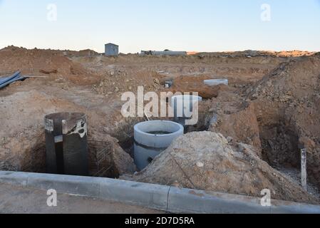 Laying concrete manholes and heating drain pipes and for stormwater system in trench at construction site. Sewerage manhole and pipes line under const Stock Photo