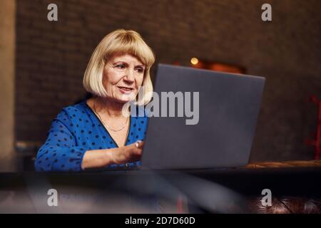 Portrait of senior woman that sits indoors in the cafe with modern laptop Stock Photo