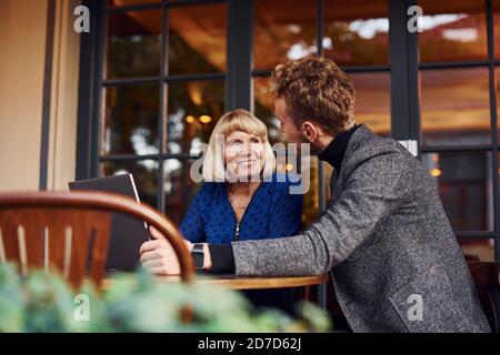 Young guy in formal clothes have a business talk with old woman in cafe Stock Photo