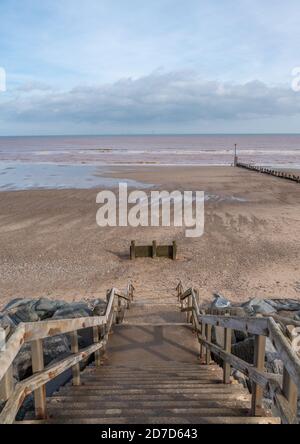 Stairs leading down to a sandy beach with the tide our and the sea in the distance. Stock Photo