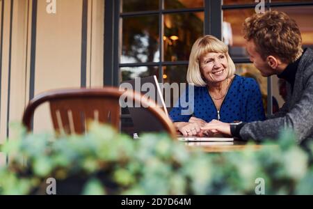 Young guy in formal clothes have a business talk with old woman in cafe Stock Photo