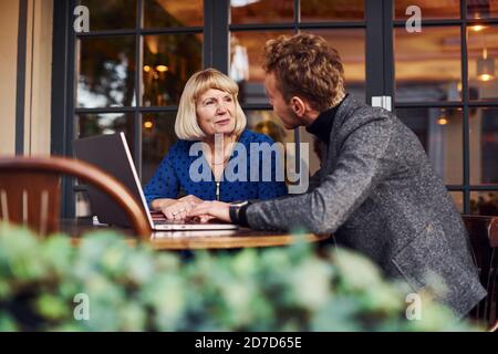 Young guy in formal clothes have a business talk with old woman in cafe Stock Photo