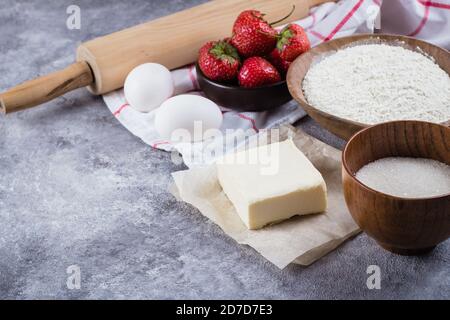 Baking ingredients for cake, pie, shortbread pastry: flour, eggs, sugar, butter, rolling pin and on gray concrete table background. Top view, copy spa Stock Photo