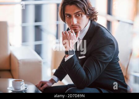 Sits on the sofa. Portrait of handsome young businessman in black suit and tie Stock Photo